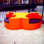 Twins — Affordance, an orange double seat with black cushions, in a Paris square